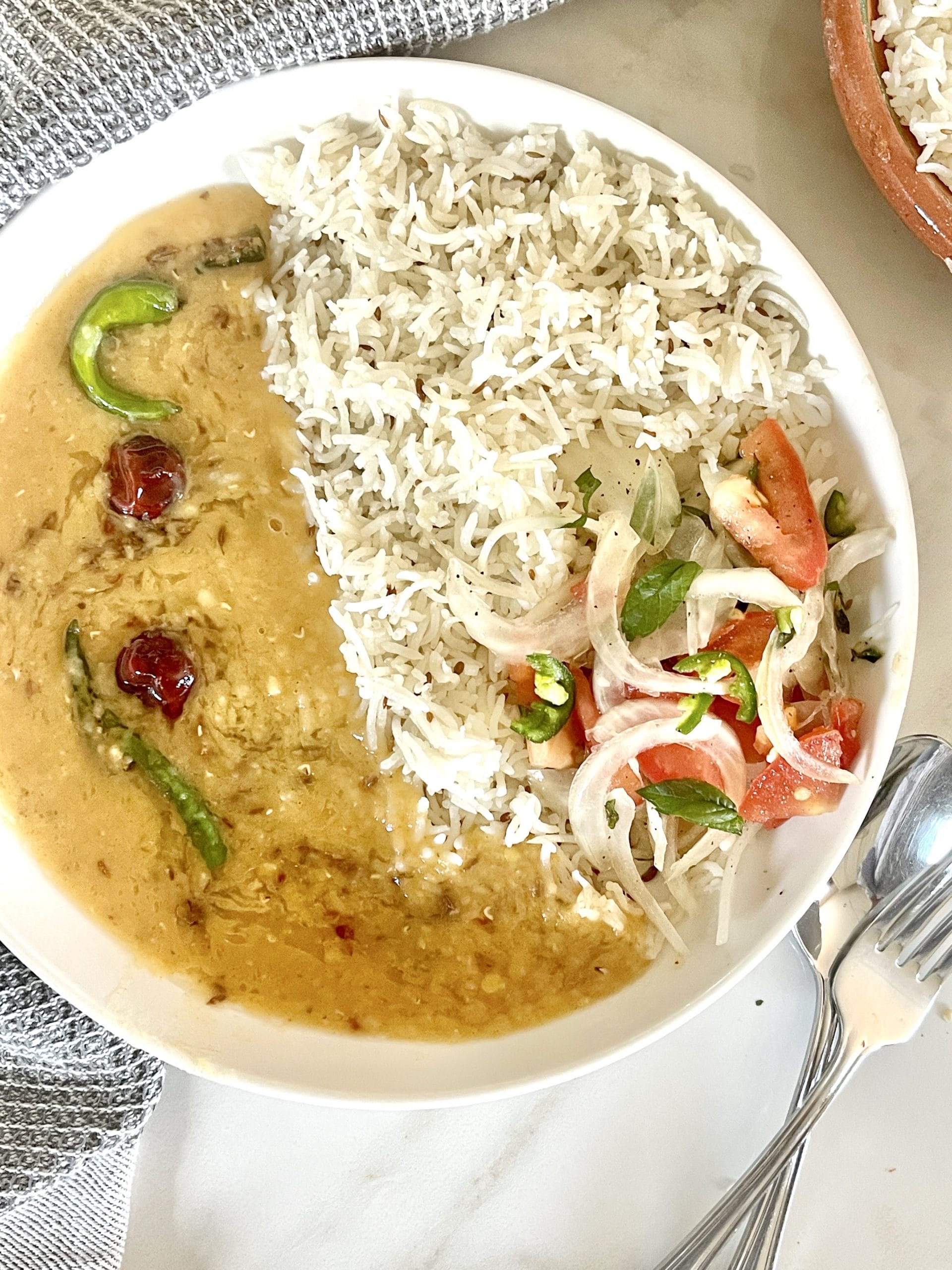 Masoor Dal served in a bowl topped with garlic tarka and chilies wIth the side of Kachoomar Salad