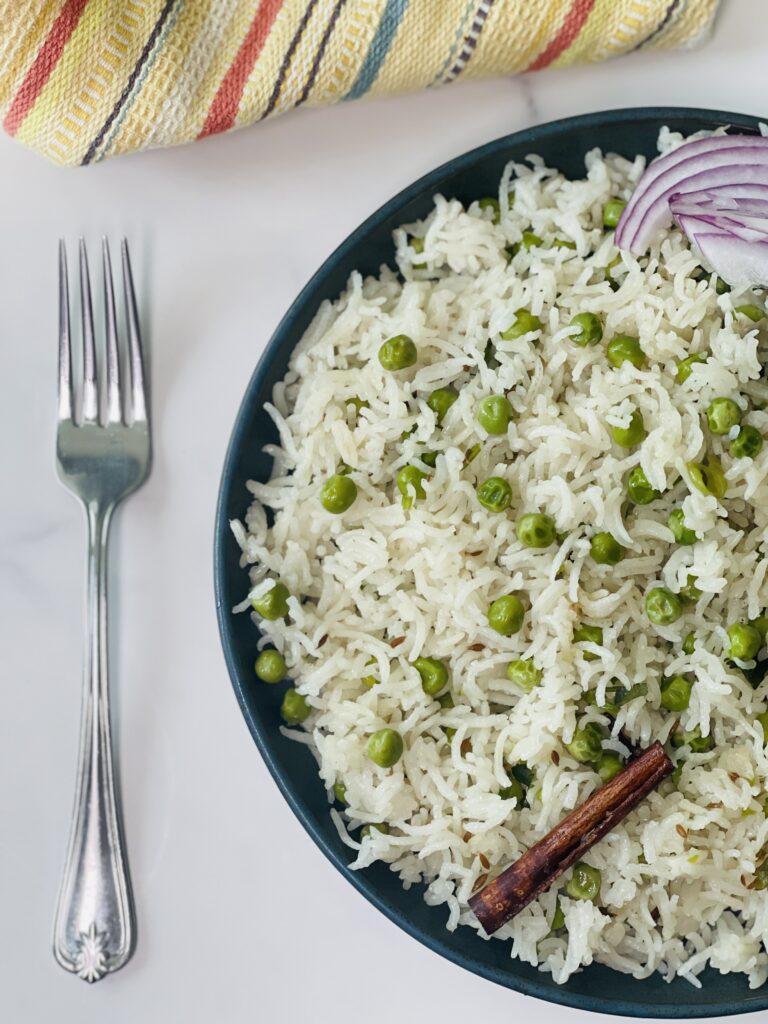 Matar Pulao Serving with a fork on a blue plate with an onion on the side