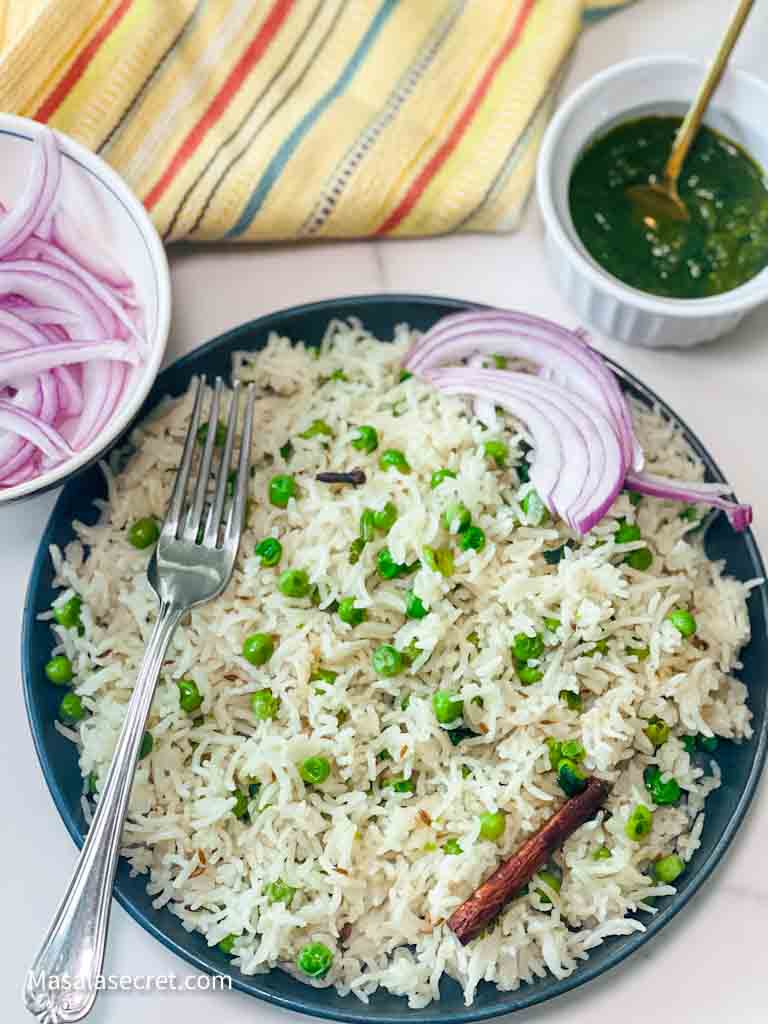 Matar Pulao  is served on a blue plate with green chutney and red onions on the side.