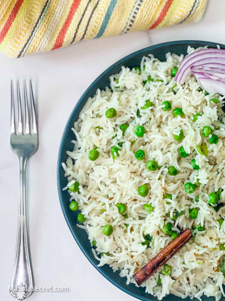 Matar Pulao Serving with a fork on a blue plate with an onion on the side