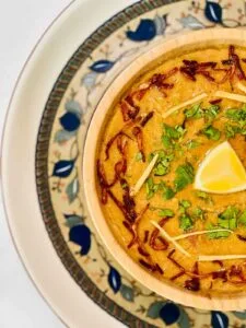 In a bowl, chicken rashi dar haleem is served with fried onion and julian cut